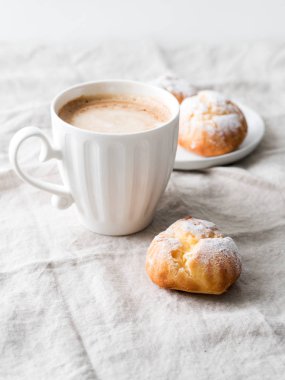 Kek profiterol bardak latte ile beyaz tabakta pudra şekeri serpilir