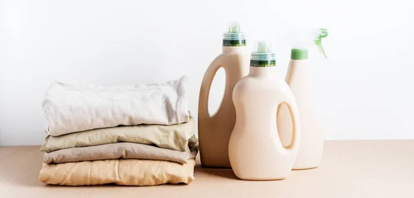 Pile of folded clean clothes with Eco Design bottles packaging for mock up of detergent for laundry on white background. Space for text. Bioorganic product layout.