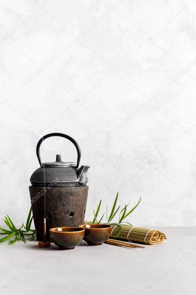 Simple still life with tea set, scattered tea, bamboo Mat, sticks, incense. Asian background with space for text.