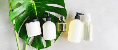 Cilt kremi, serum, yağ, şampuan, saç kremi, saç kremi, parfüm ve yeşil yapraklı gri arka planda parfüm için makyaj malzemeleri. Doğal güzellik ürünü konsepti.