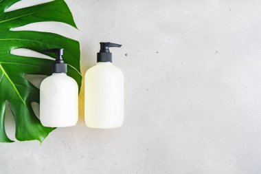 Cilt kremi, şampuan ve yeşil yapraklı gri arka planda saç kremi için iki adet boş etiket şişesi. Doğal güzellik ürünü konsepti.