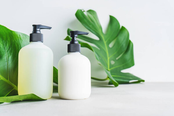 Косметический набор из двух пустых бутылок этикетки для макета упаковки крема для кожи, шампуня, кондиционера на сером фоне с зелеными листьями. Концепция натуральной красоты
.