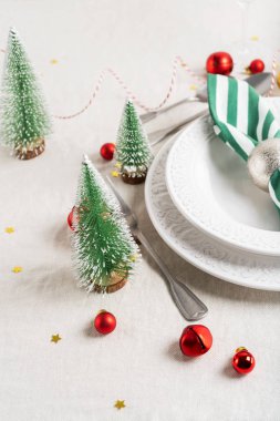 Beyaz tabaklar, çatal bıçak takımı, peçete ve Noel süsüyle Noel sofrası, keten masa örtüsünün üzerinde fotokopi alanı olan ağaç oyuncakları. Kış, yeni yıla özel konsept masa servisi.