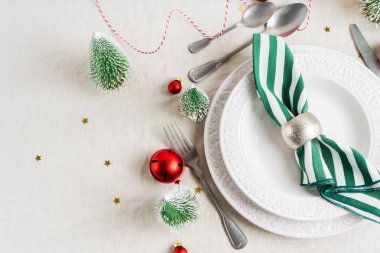 Beyaz tabaklar, çatal bıçak takımı, peçete ve Noel süsüyle Noel sofrası, keten masa örtüsünün üzerinde fotokopi alanı olan ağaç oyuncakları. Kış, yeni yıla özel konsept masa servisi.
