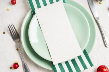 İçinde menü ya da gümüş çatal bıçaklı beyaz tabaklar için davetiye olan güzel bir Noel sofrası, keten masa örtüsü arka planında şenlikli klasik dekorasyon. Tatil planı.