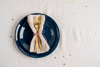 Mavi tabakların yakın görüntüsü, masa örtüsü üzerine kurulmuş kutlama masası için peçetedeki altın çatal bıçak seti. Kopya alanı olan yeni yıl düzeni için