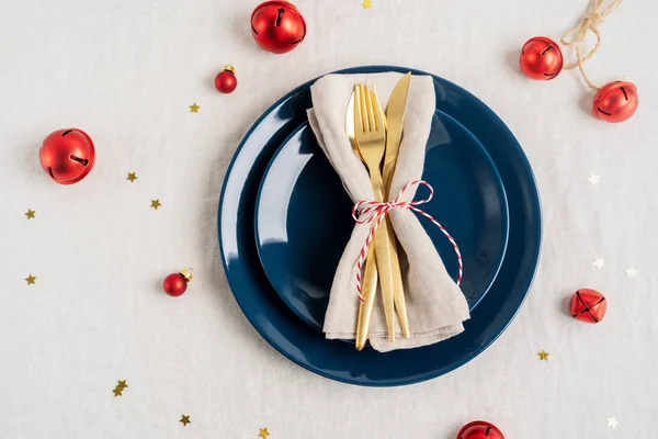 Christmas table setting. Holiday Decorations with tree toys, shiny confetti, golden cutlery on light linen tablecloth with copy space. Holiday layout.