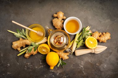 Making healthy antioxidant and anti-inflammatory ginger tea with fresh ginger, lemongrass, sage, honey and lemon on dark background with copy space. Top view. clipart
