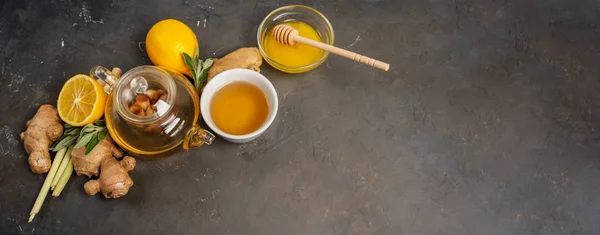 Making healthy antioxidant and anti-inflammatory ginger tea with fresh ginger, lemongrass, sage, honey and lemon on dark background with copy space.