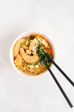 Baharatlı karides kasesi, pirinç, yosun ve susam tohumlu Asya yemekleri. Beslenme çantasında beyaz çubuklarla birlikte avokado. Sağlıklı deniz ürünleri yemeği. Diyet yemek. Kopyalama alanı olan üst görünüm.