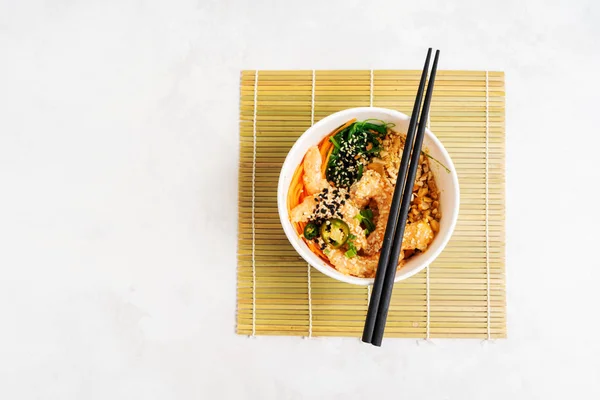 Asian food background with Spicy Shrimp Poke Bowl with rice, seaweeds and sesame seeds, avocado with chopsticks on white. Buddha bowl. Healthy seafood lunch. Diet food. Top view with copy space.
