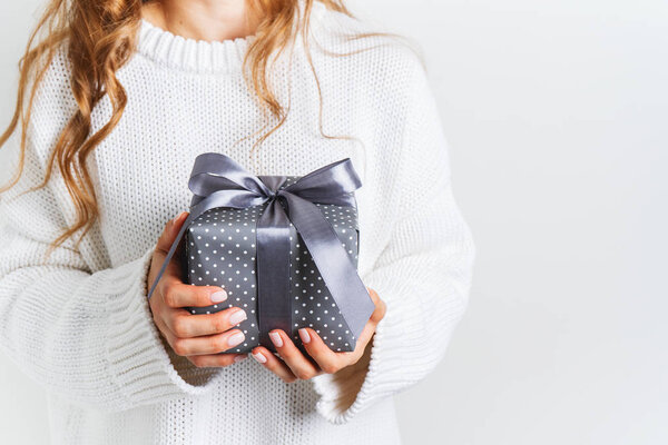 Женщина в шерстяном белом свитере держит подарочную коробку с бантиком. Рождественская праздничная планировка. Макет к Новому году
.