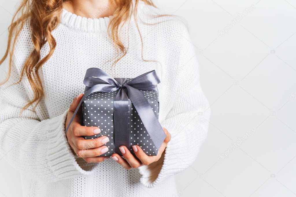 Female in woolen white sweater holding a gift box with a bow. Christmas festive layout. Mockup for New Year.