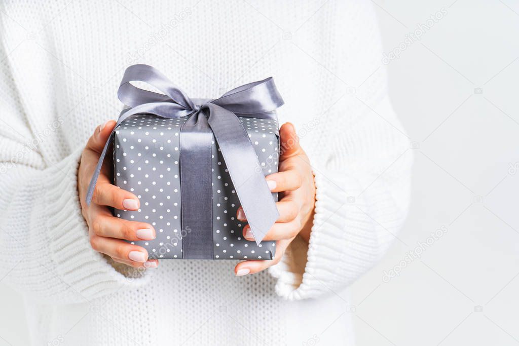 Female in woolen white sweater holding a gift box with a bow. Christmas festive layout. Mockup for New Year.