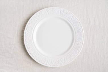 Keten masa örtüsünün üzerinde boş seramik tabağın fotokopi alanı olan üst görüntüsü. Yemek masası servisini kabul et. 