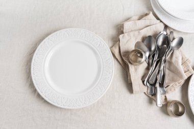 Çatal bıçak takımı, peçeteler, peçete halkaları ve tabaklarda boş bir masa örtüsü. Festival tablosu için hazırlama.