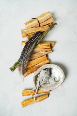Smudge kit for spiritual practices with natural elements: Palo Santo sticks, dried white sage, Guinea Fowl feather, crystals, sea pearl shell Abalone on a light background. Balancing the soul.