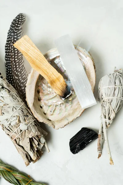 Smudge kit for spiritual practices with natural elements: Palo Santo sticks, dried white sage, Guinea Fowl feather, crystals, sea pearl shell Abalone on a light background. Balancing the soul.
