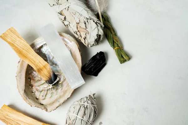 Smudge kit for spiritual practices with natural elements: Palo Santo sticks, dried white sage, Guinea Fowl feather, crystals, sea pearl shell Abalone on a light background. Balancing the soul.