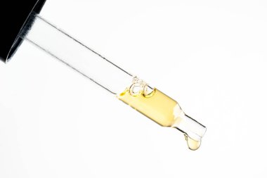 Beyaz arka plana damlayan sıvı damlalı kozmetik pipeti. Makro manzara şeffaf cam pipet. Güzellik kavramı, aromaterapi yağı, ilaç, aşı geliştirme.
