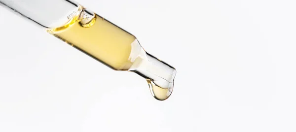 Beyaz arka plana damlayan sıvı damlalı kozmetik pipeti. Makro manzara şeffaf cam pipet. Güzellik kavramı, aromaterapi yağı, ilaç, aşı geliştirme.