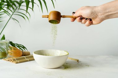 Yeşil çay tozu seramik bir kaseye dökülüyor. Beyaz arka planda geleneksel kibrit çöpleriyle Japon latte çayı yapıyorum..