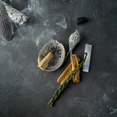 Doğal elementlerle ruhani uygulamalar için leke kiti: Palo Santo çubukları, kurutulmuş beyaz adaçayı, Gine Fowl tüyü, kristaller, siyah arka planda deniz kabuğu deniz tarağı. Ruhu dengelemek. 