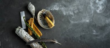 Doğal elementlerle ruhani uygulamalar için leke kiti: Palo Santo çubukları, kurutulmuş beyaz adaçayı, Gine Fowl tüyü, kristaller, siyah arka planda deniz kabuğu deniz tarağı. Ruhu dengelemek. 