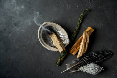 Doğal elementlerle ruhani uygulamalar için leke kiti: Palo Santo çubukları, kurutulmuş beyaz adaçayı, Gine Fowl tüyü, kristaller, siyah arka planda deniz kabuğu deniz tarağı. Ruhu dengelemek. 