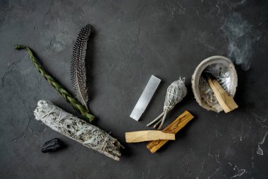 Doğal elementlerle ruhani uygulamalar için leke kiti: Palo Santo çubukları, kurutulmuş beyaz adaçayı, Gine Fowl tüyü, kristaller, siyah arka planda deniz kabuğu deniz tarağı. Ruhu dengelemek. 