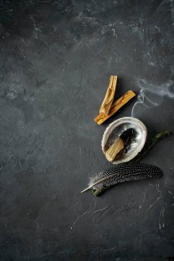 Doğal elementlerle ruhani uygulamalar için leke kiti: Palo Santo çubukları, kurutulmuş beyaz adaçayı, Gine Fowl tüyü, kristaller, siyah arka planda deniz kabuğu deniz tarağı. Ruhu dengelemek. 