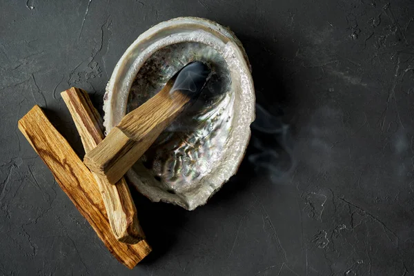 Doğal elementlerle ruhani uygulamalar için leke kiti: Palo Santo çubukları, kurutulmuş beyaz adaçayı, Gine Fowl tüyü, kristaller, siyah arka planda deniz kabuğu deniz tarağı. Ruhu dengelemek. 