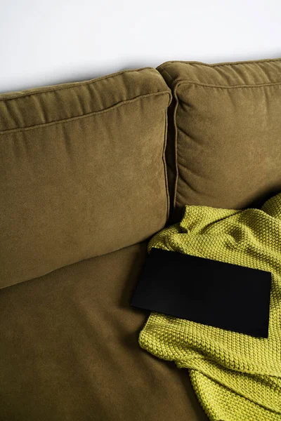 Fabric velvet green sofa with green soft knitted blanket plaid and laptop. Copy space for text, mockup with copy space. Stay ay home. Remote work from a cozy home.