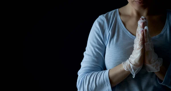 Woman prays with faith to GOD. Religion care during the pandemic crisis. Hands in disposable gloves are folded in prayer. Online church worship.