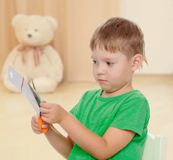 Мальчик режет ножницами картон — стоковое фото