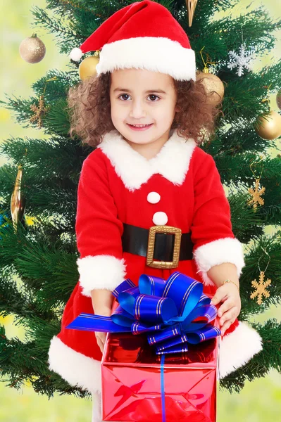 Klein meisje in de buurt van de kerstboom met een geschenk in zijn handen Stockfoto