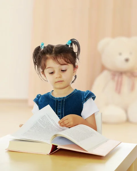 Klein meisje dat een boek aan tafel leest. — Stockfoto