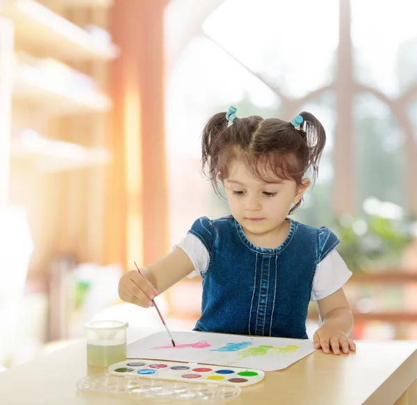 Mała dziewczynka maluje farbami przy stole. — Zdjęcie stockowe
