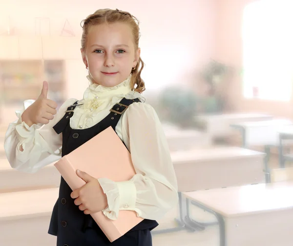 Školačka dívka s knihou v ruce ukazuje palec. — Stock fotografie