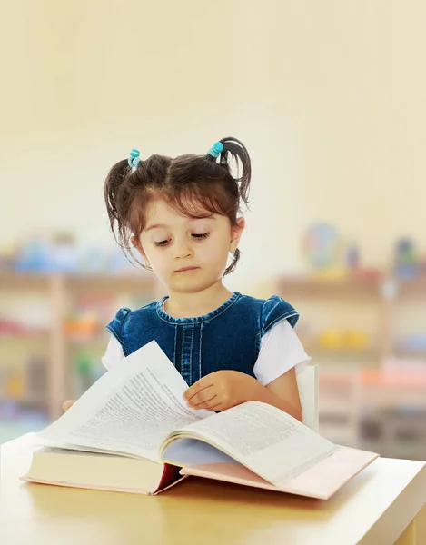 Klein meisje dat een boek aan tafel leest. — Stockfoto