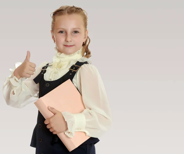 Girl schoolgirl with a book in hand shows thumb. — Stock Photo, Image