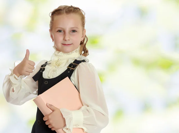 Flicka skolflicka med en bok i handen visar tummen. — Stockfoto