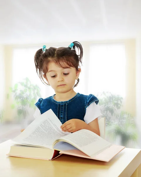 테이블에서 책을 읽고 있는 어린 소녀. — 스톡 사진