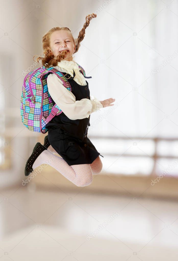 Girl schoolgirl with a satchel behind shoulders jumps