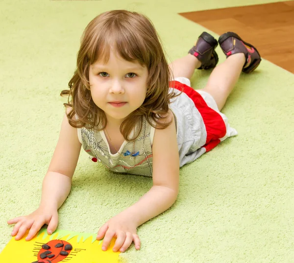 Маленькая девочка лежит на полу и смотрит на рисунок — стоковое фото