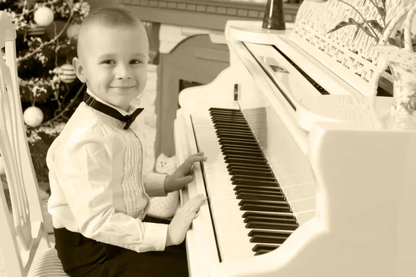 Mały chłopiec gra na biały fortepian. — Zdjęcie stockowe