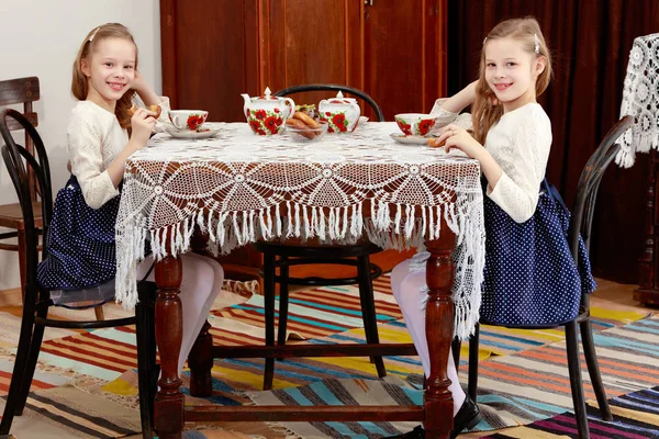Niñas gemelas bebiendo té en una mesa antigua con una mantel de encaje —  Fotos de Stock