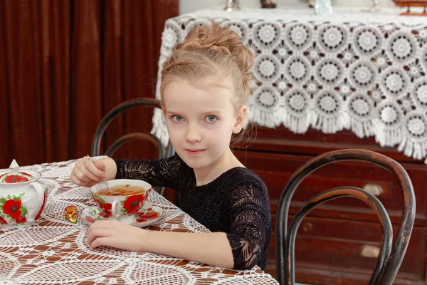 Красивая маленькая девочка пьет чай за столом . — стоковое фото