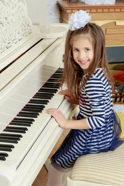 Flicka leende sitter bakom tangenterna av en stor vit piano. — Stockfoto