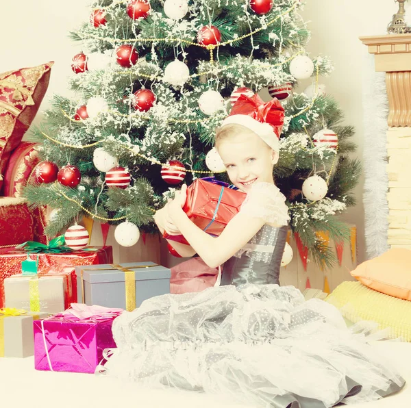Little girl sitting near Christmas tree with a big gift. Royalty Free Stock Images